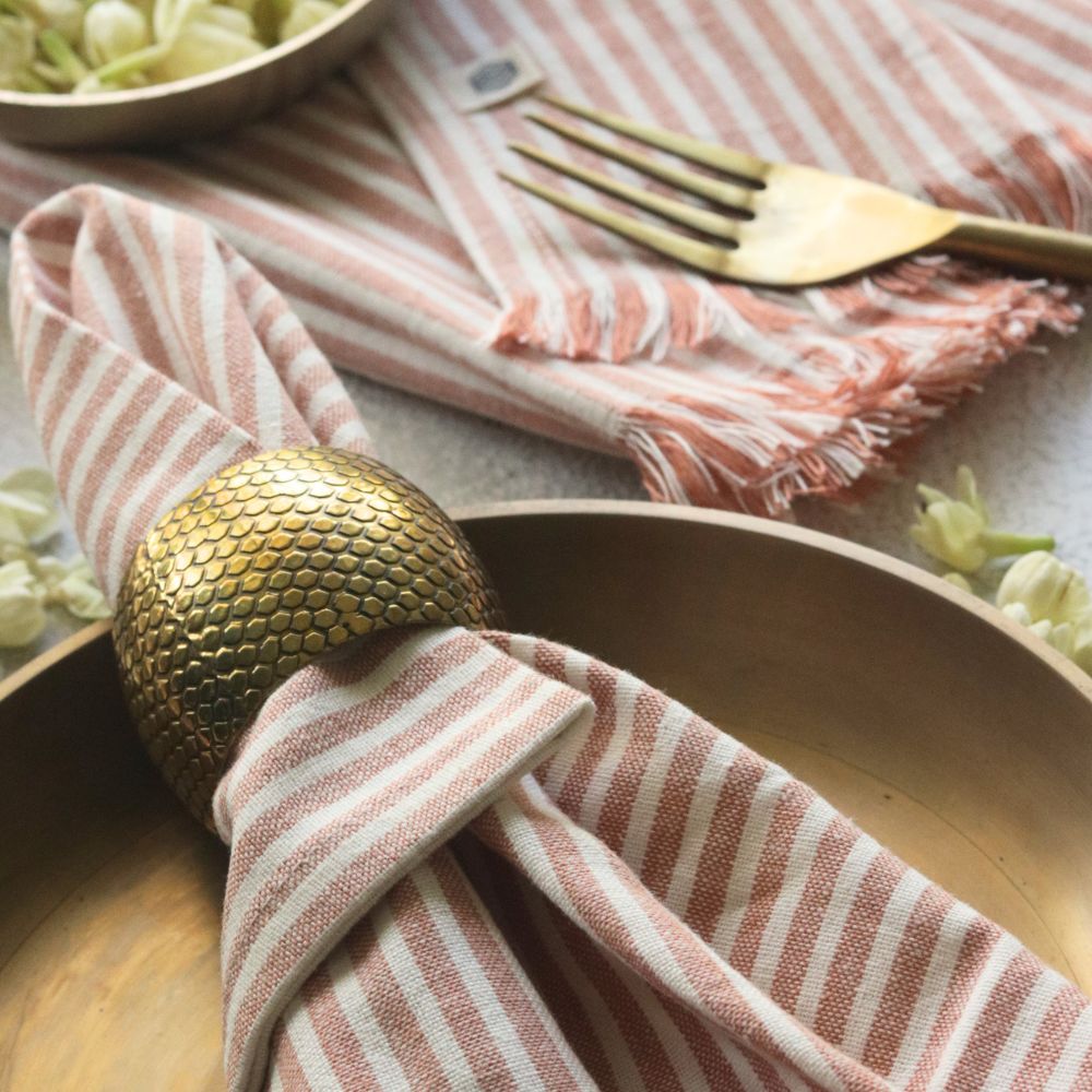 Dusty rose striped cotton napkin with fringe, folded on table setting