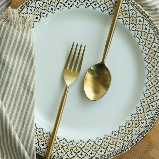 Matte gold dinner spoon and fork arranged on a patterned plate