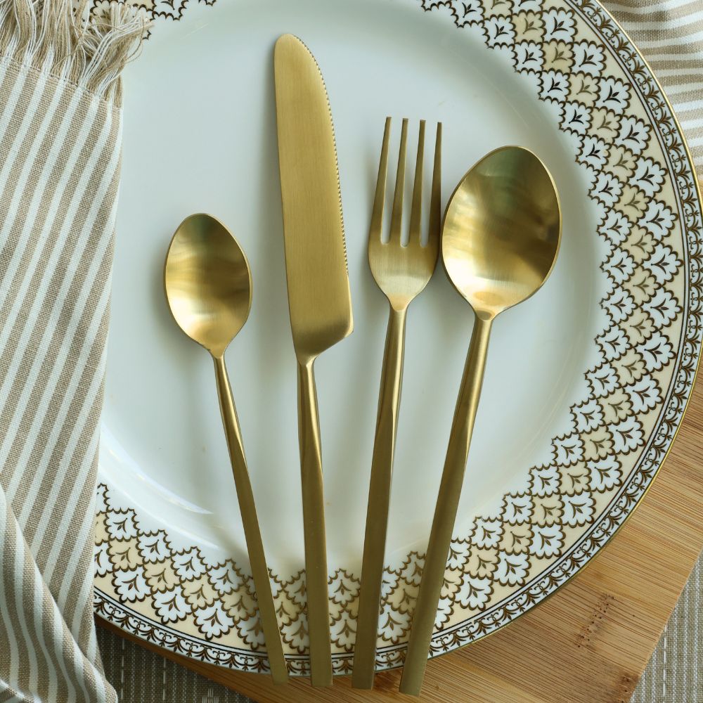Four-piece matte gold cutlery set arranged on a plate