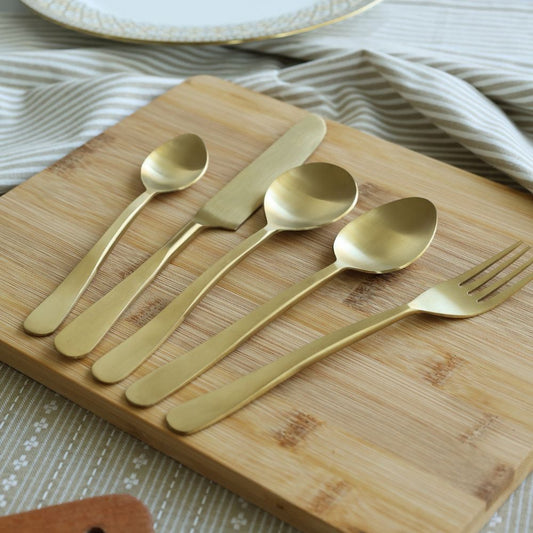 Five-piece matte gold cutlery set arranged on a board