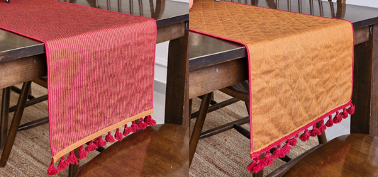 Red and mustard quilted table runners with tassels on wooden dining table.