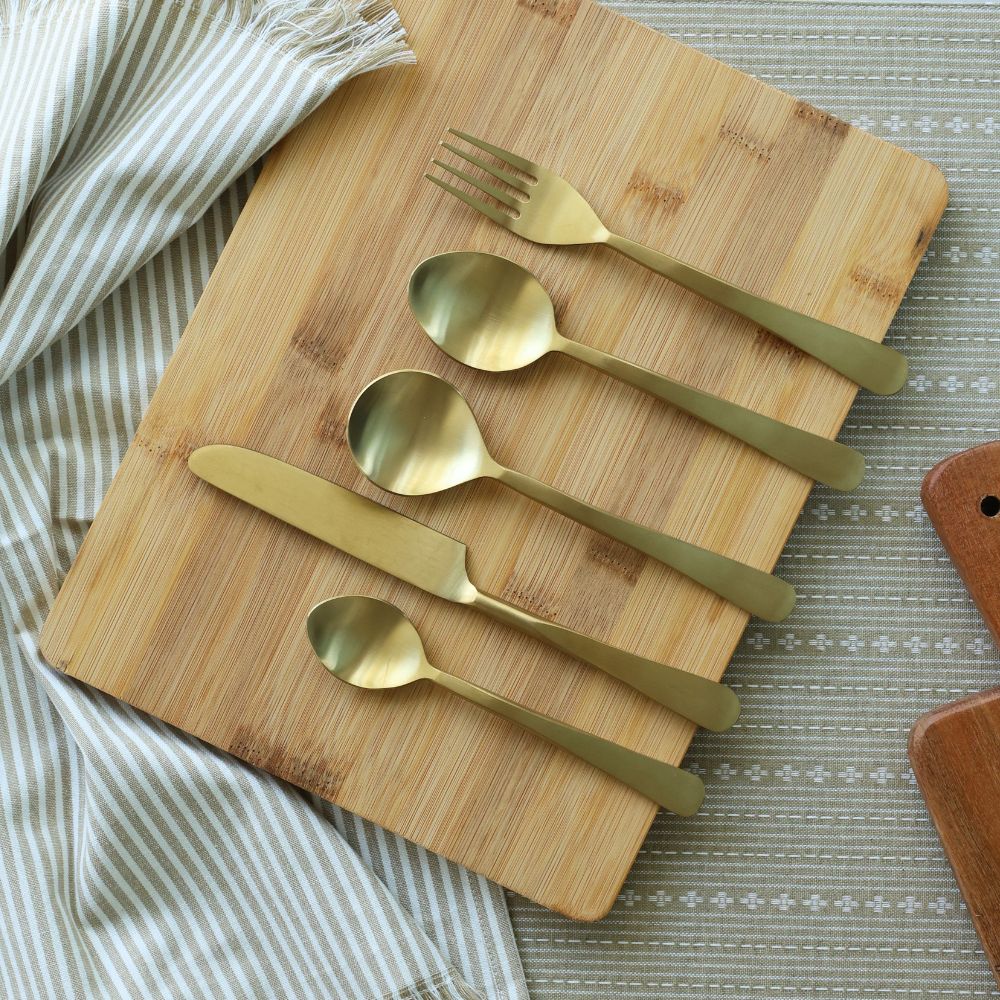 Five matte gold utensils arranged in a row on a board