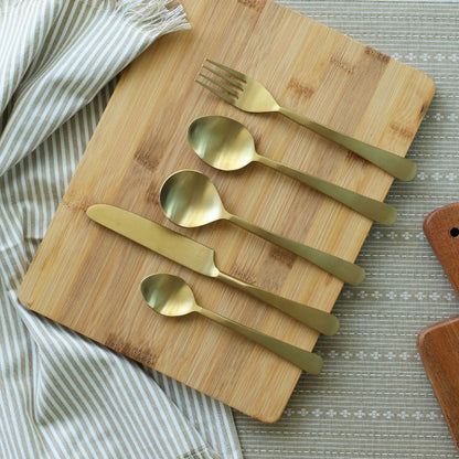 Five matte gold utensils arranged in a row on a board