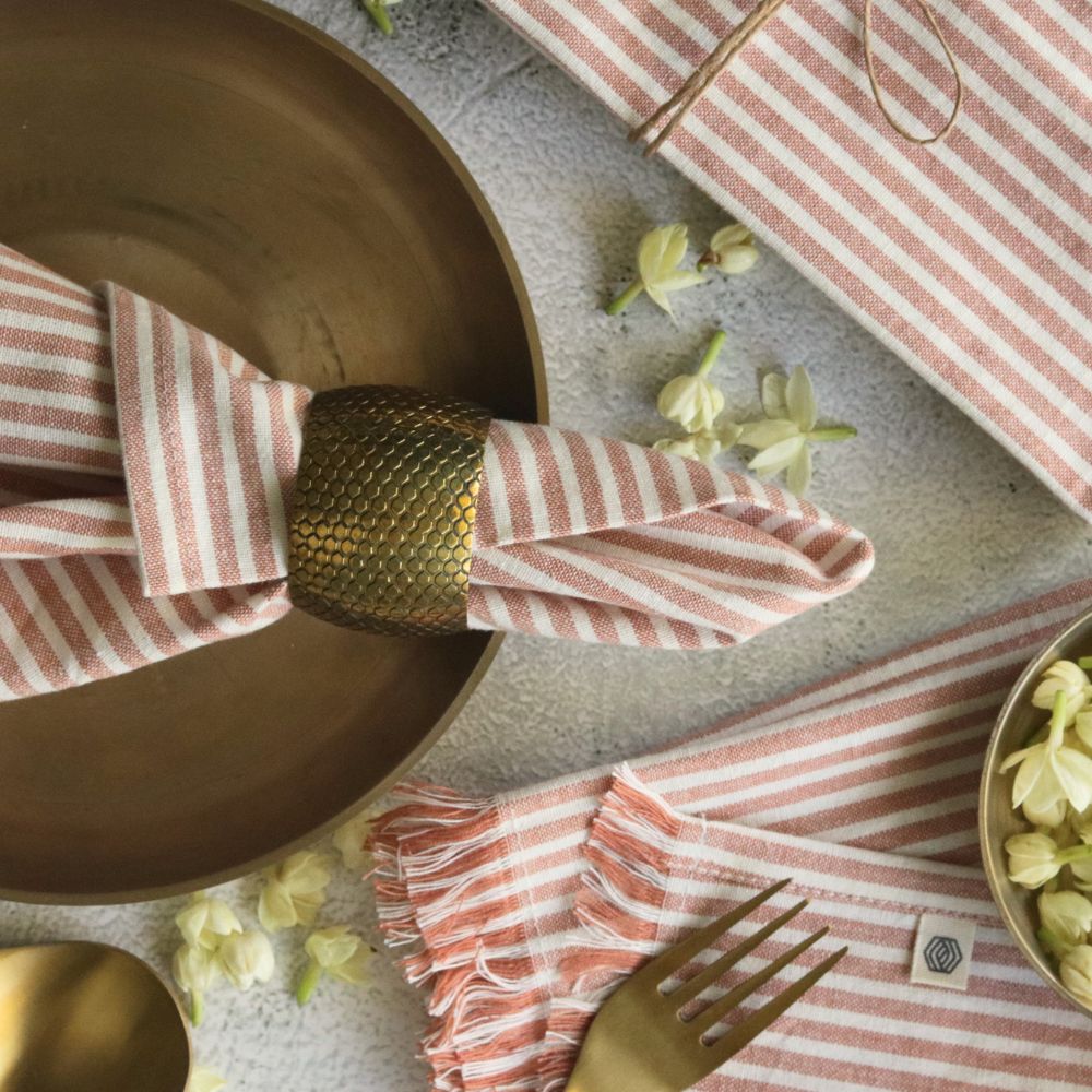 Dusty rose and white striped napkin with fringe, folded and secured with gold band