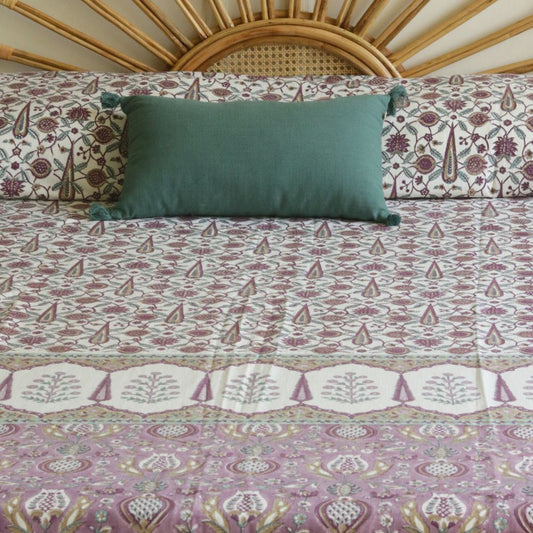 Mauve and white patterned bed cover with repeating medallion motifs; green pillow