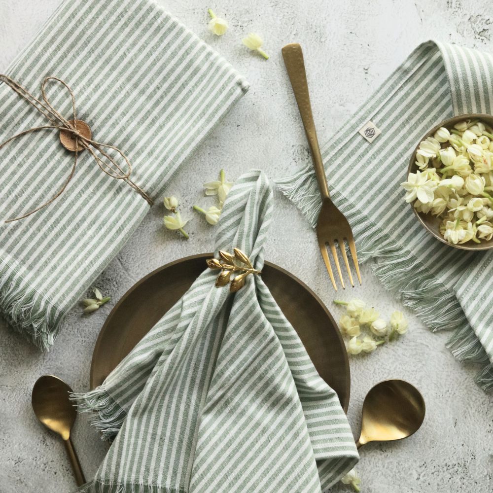 Folded sage green striped cotton napkin with tied center knot and fringed trim