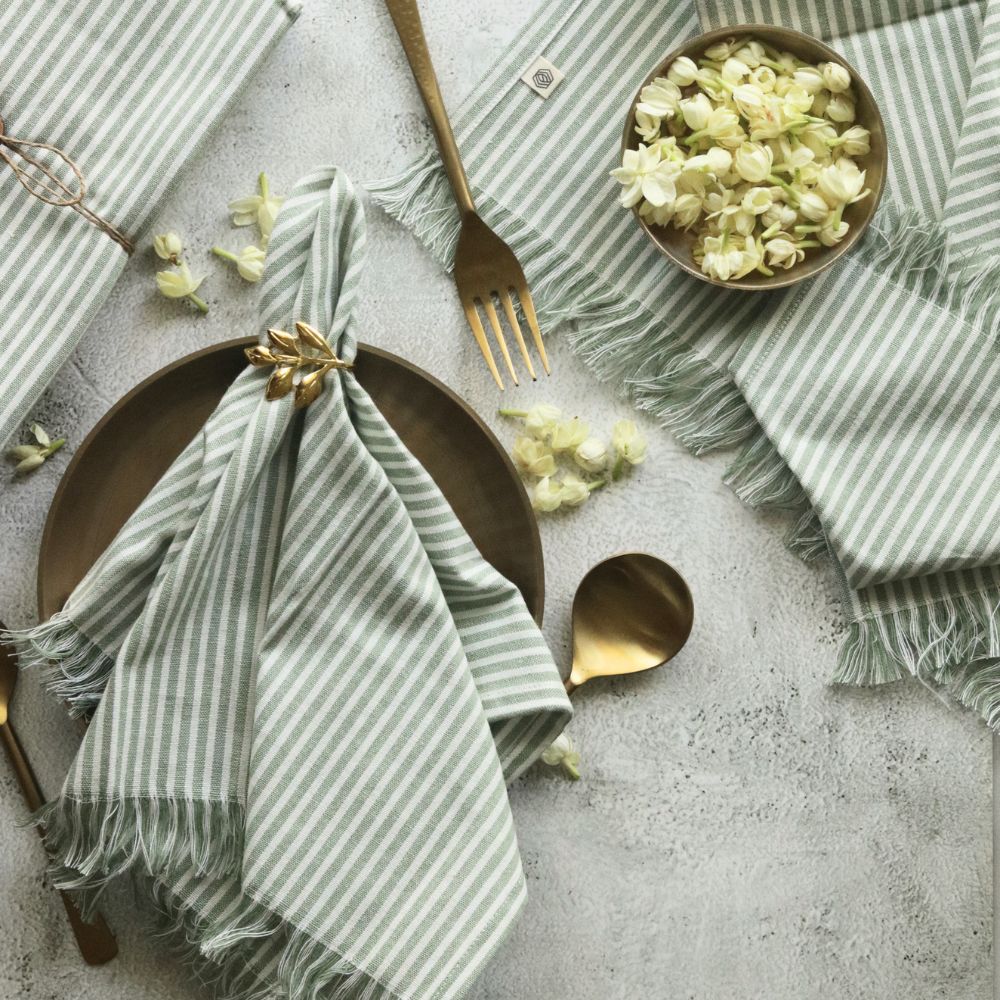 Sage green striped cotton napkin, pleated and fringed, tied with gold bow