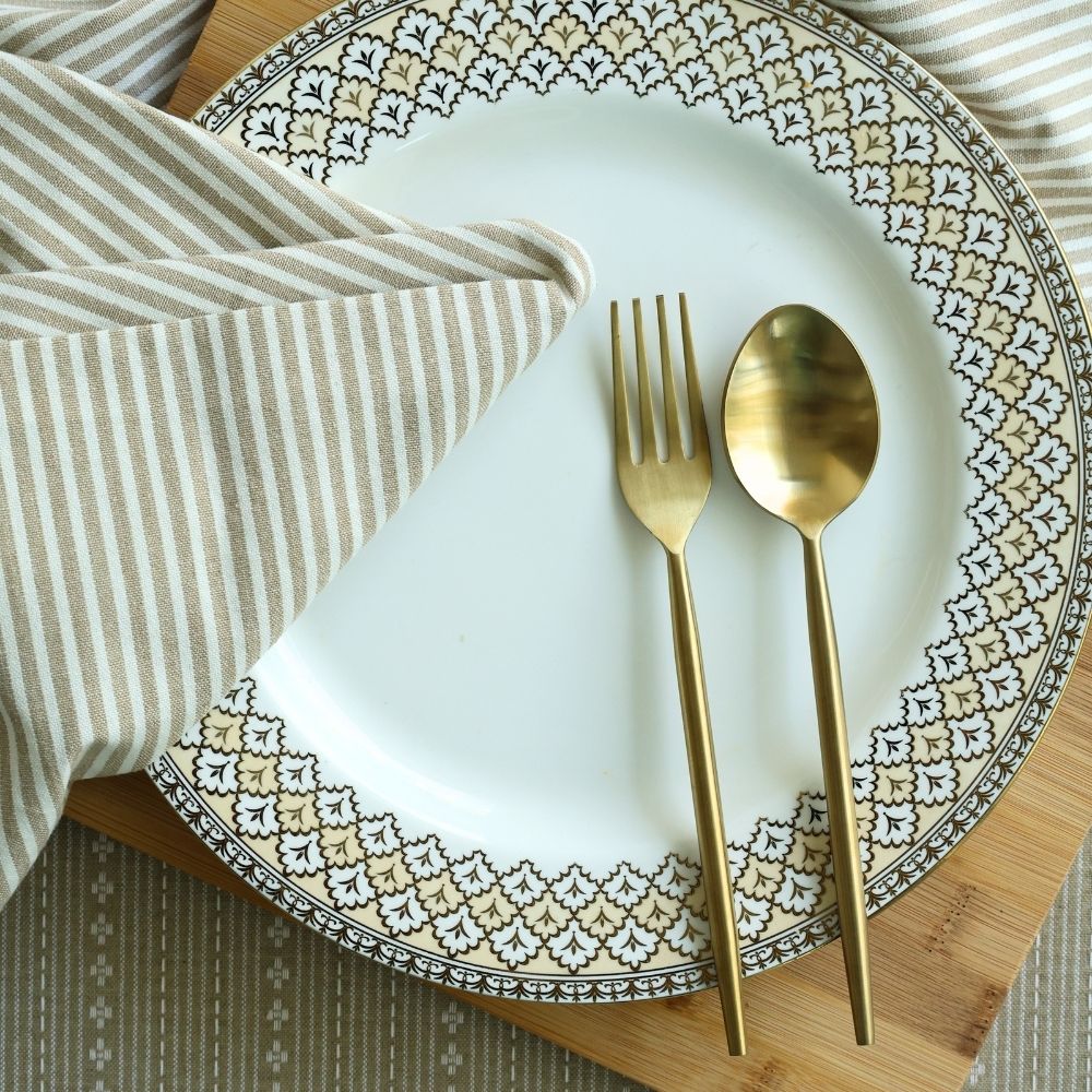 Matte gold dinner spoon and fork beside a folded striped napkin