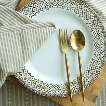 Matte gold dinner spoon and fork beside a folded striped napkin