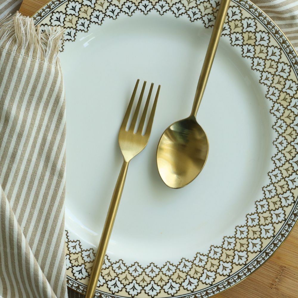 Matte gold dinner spoon and fork arranged on a patterned plate