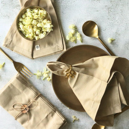 Beige cotton table napkins with gold leaf ring bow detail, neatly folded