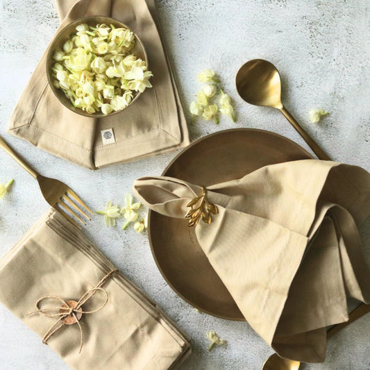 Beige cotton table napkins with gold leaf ring bow detail, neatly folded