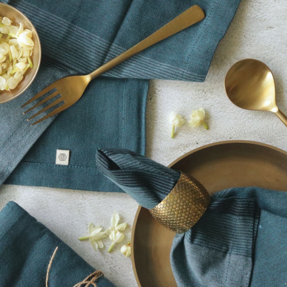 Aegean blue cotton napkin, folded and secured with a gold-toned holder