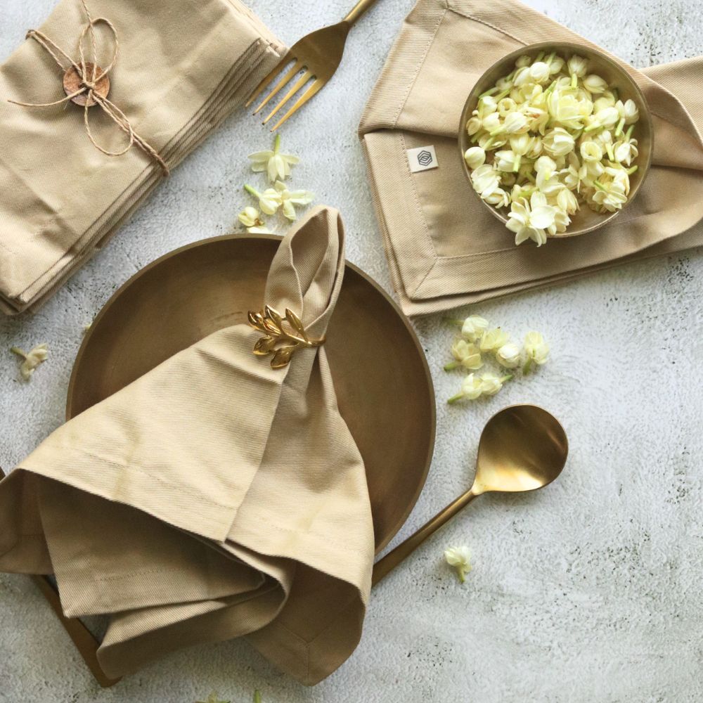 Beige cotton table napkins, folded with gold leaf bow accents