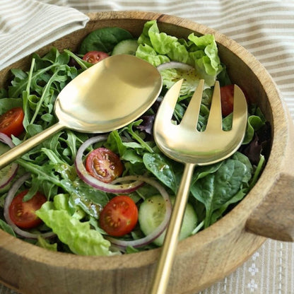 Matte gold salad servers resting in a wooden bowl of salad