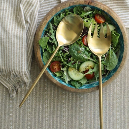 Matte gold salad servers placed over a bowl of mixed greens and vegetables