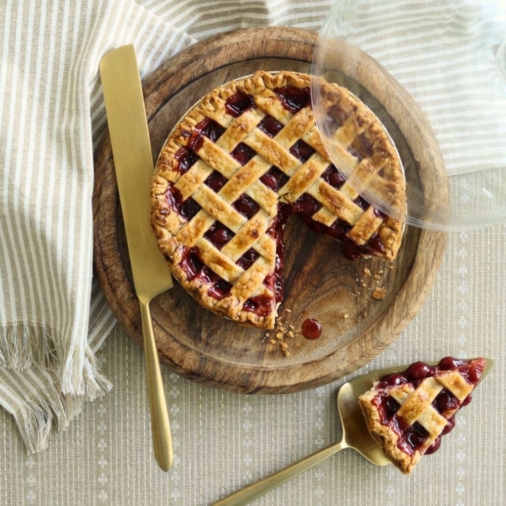 Matte gold pie server lifting a slice beside a berry pie and matching cutter.
