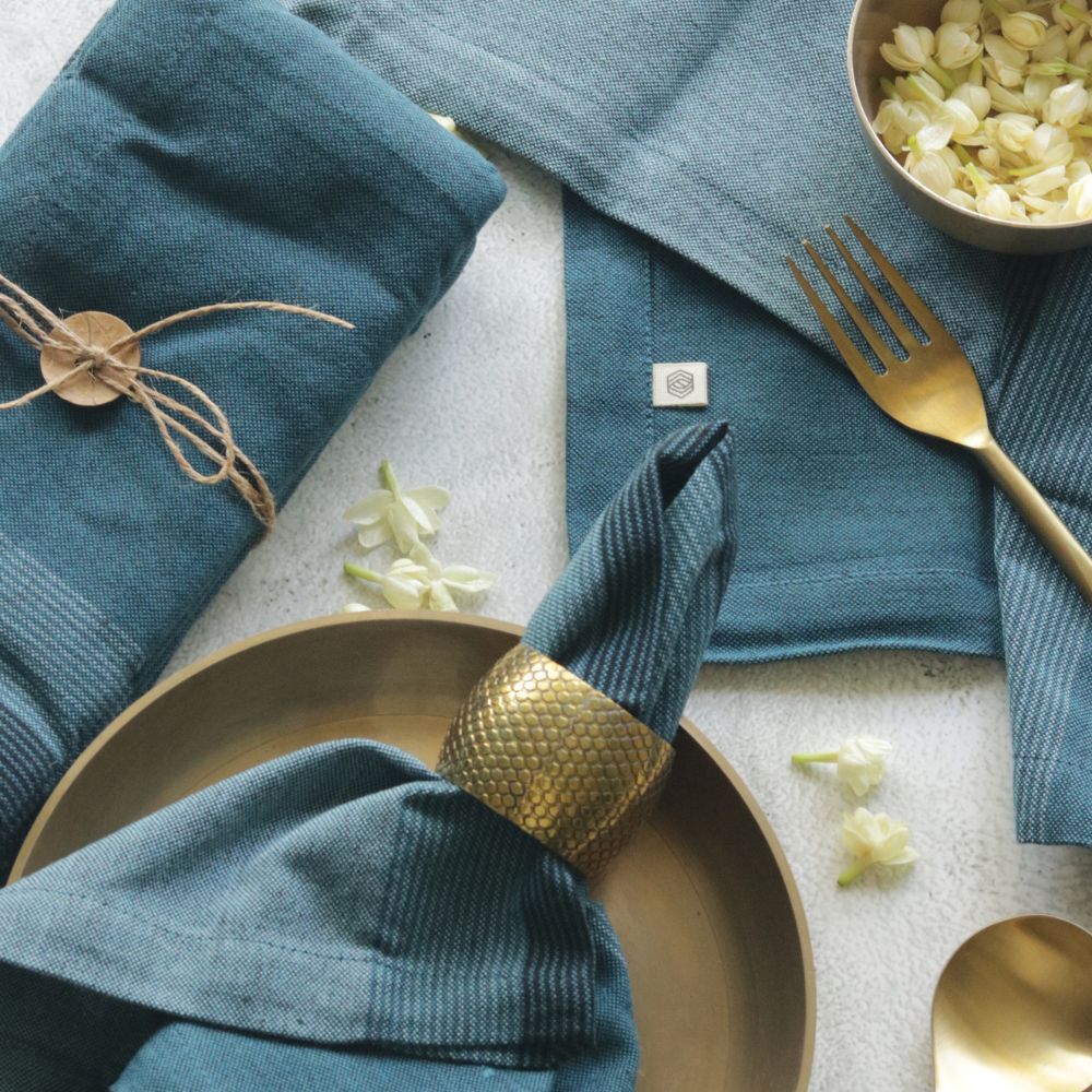 Aegean blue cotton table napkin, folded with a tied fabric band and seam detail