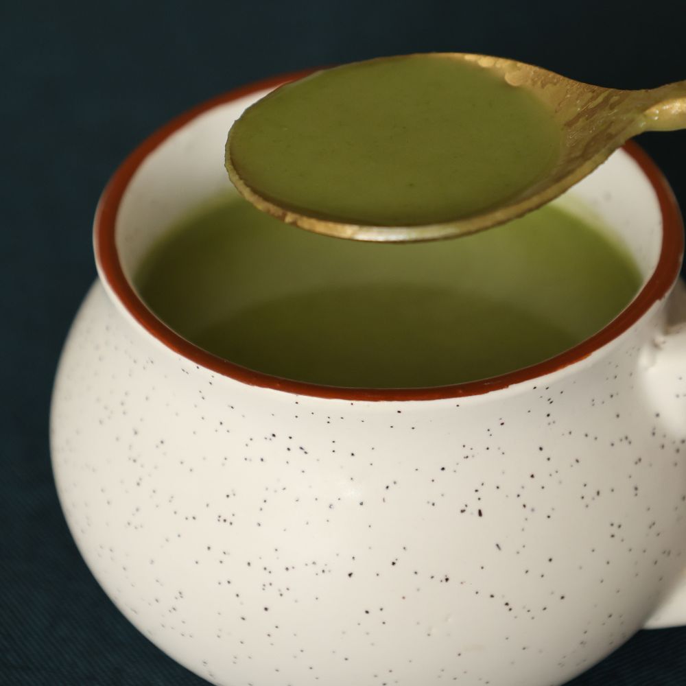 Matte gold spoon holding soup above a cup