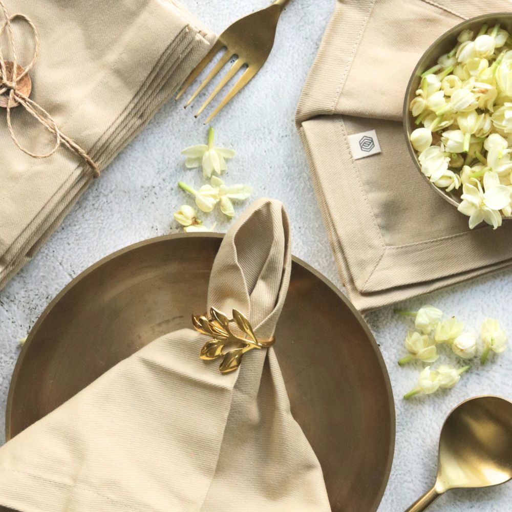 Beige cotton napkins with gold leaf bow detail, folded squarely