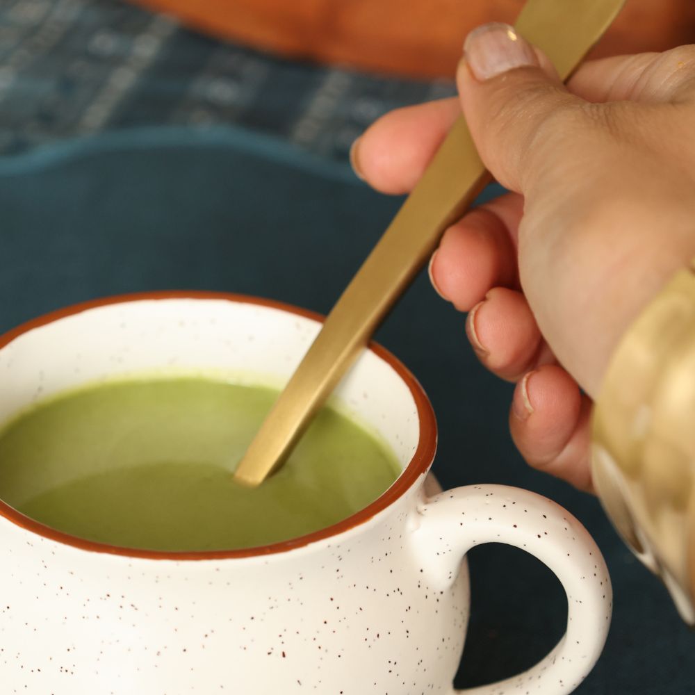 Matte gold spoon stirring soup in a cup