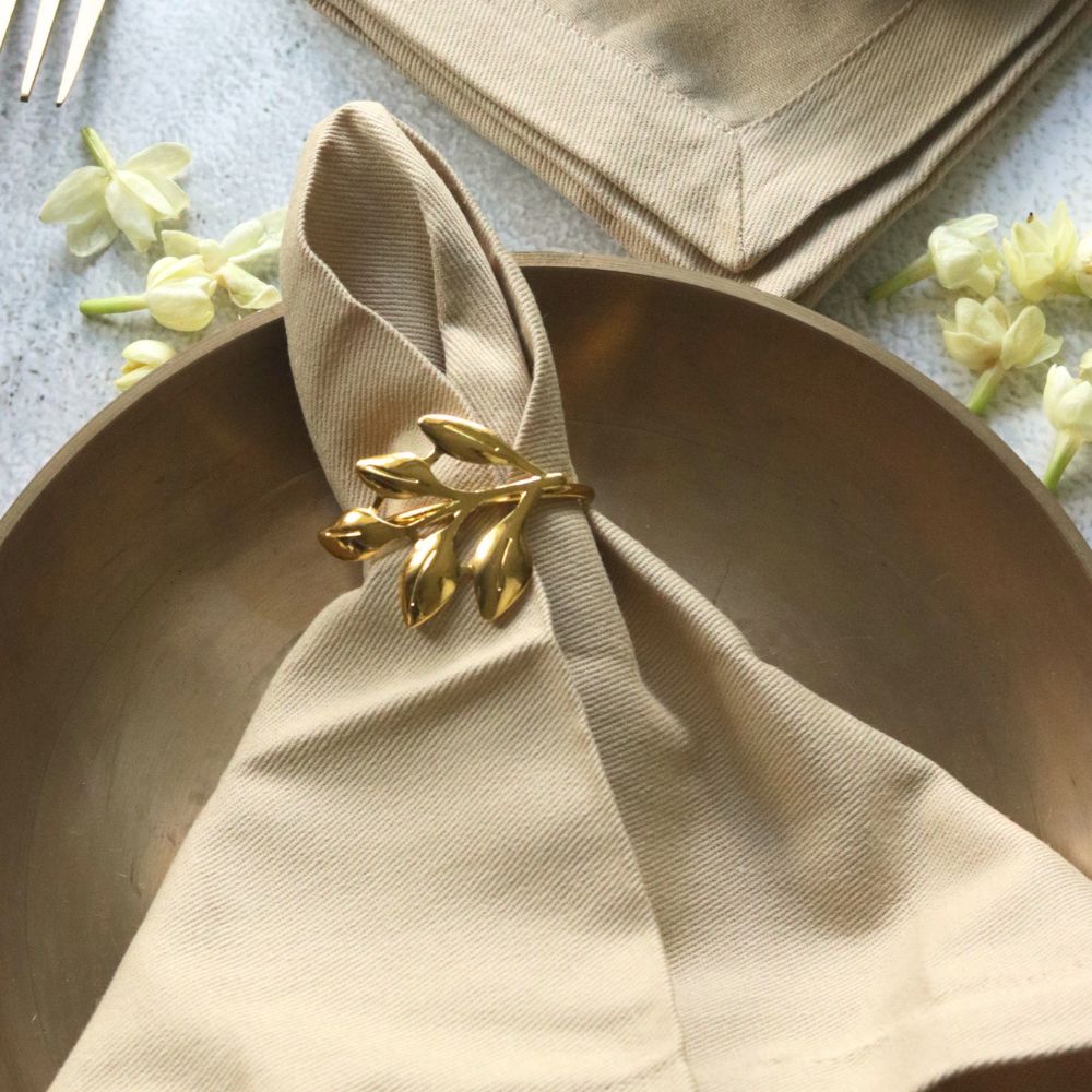 Beige cotton table napkin close-up with gold leaf bow clasp