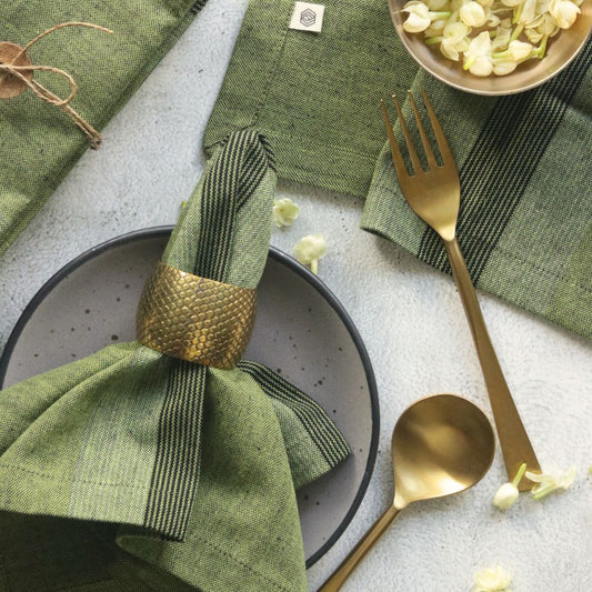 Moss green cotton table napkin, folded with dark striped band and gold napkin ring