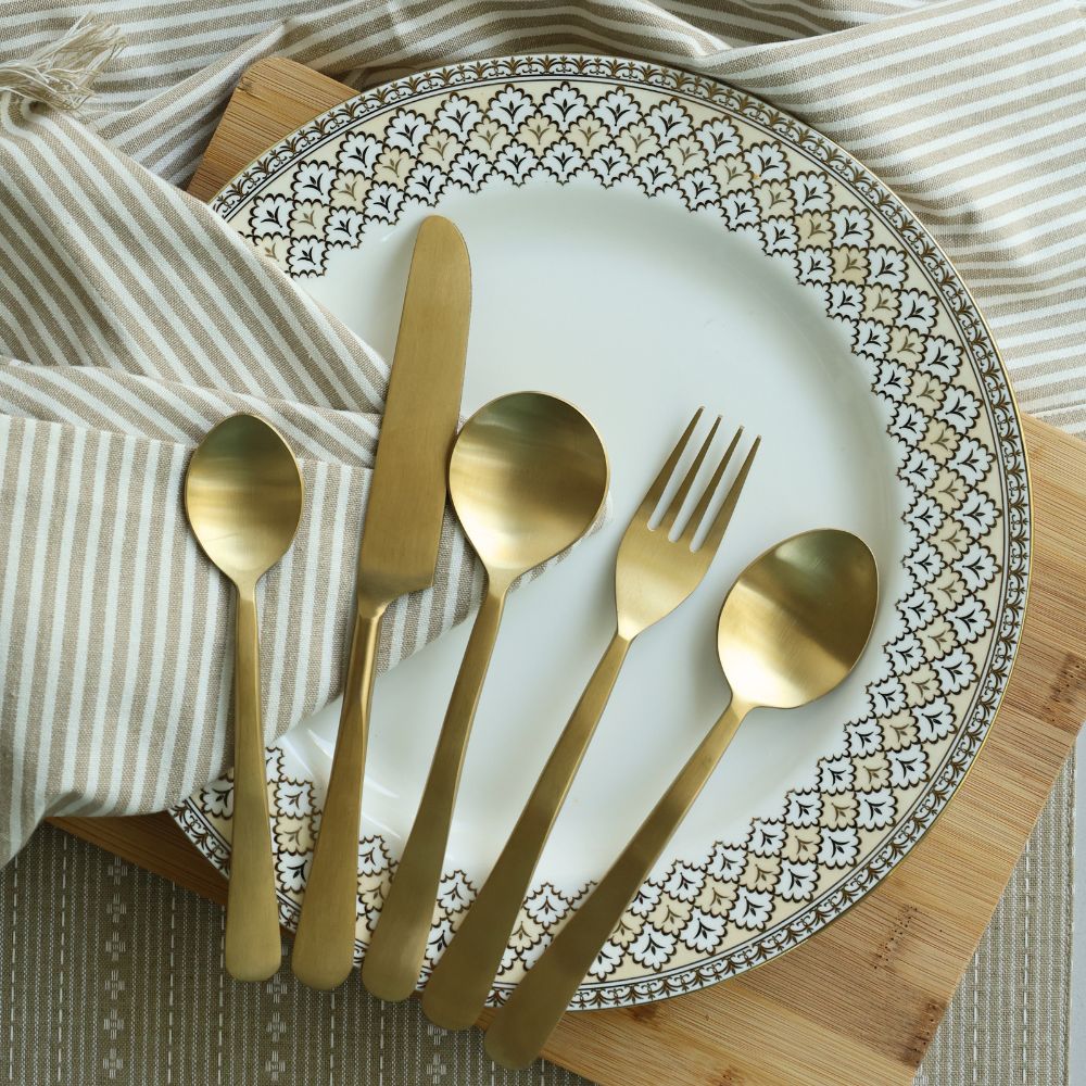 Five-piece matte gold cutlery set arranged on a plate