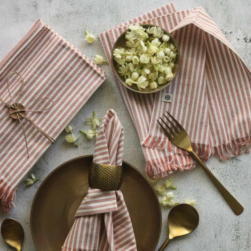 Cotton table napkins in dusty rose with white stripes and fringed hem, shown folded