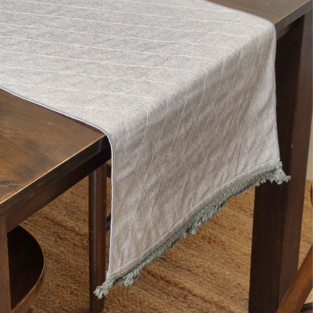 A grey textured 6 seater reversible runner draped over the edge of a dining table with tassels.