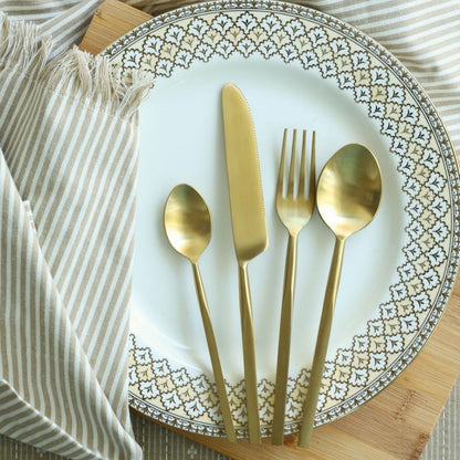 Four-piece matte gold cutlery set arranged on a decorative plate