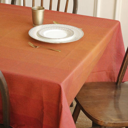 Dining table with a red tablecloth, white plate, gold fork, and cup.