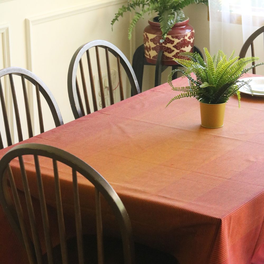 Dining table with a red tablecloth and potted plants, surrounded by chairs.