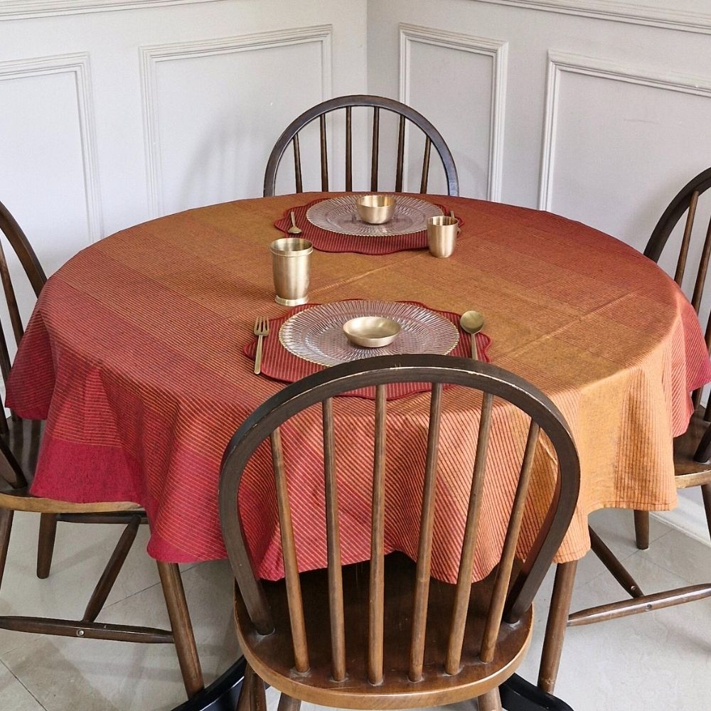 Round table with a red and orange checkered tablecloth, set with silverware and plates, against a white paneled wall.