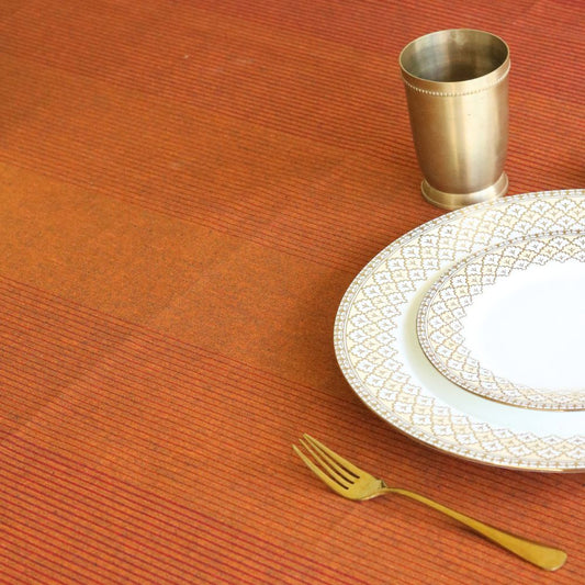 Table setting with a gold cup, plate, and fork on an orange textured tablecloth.