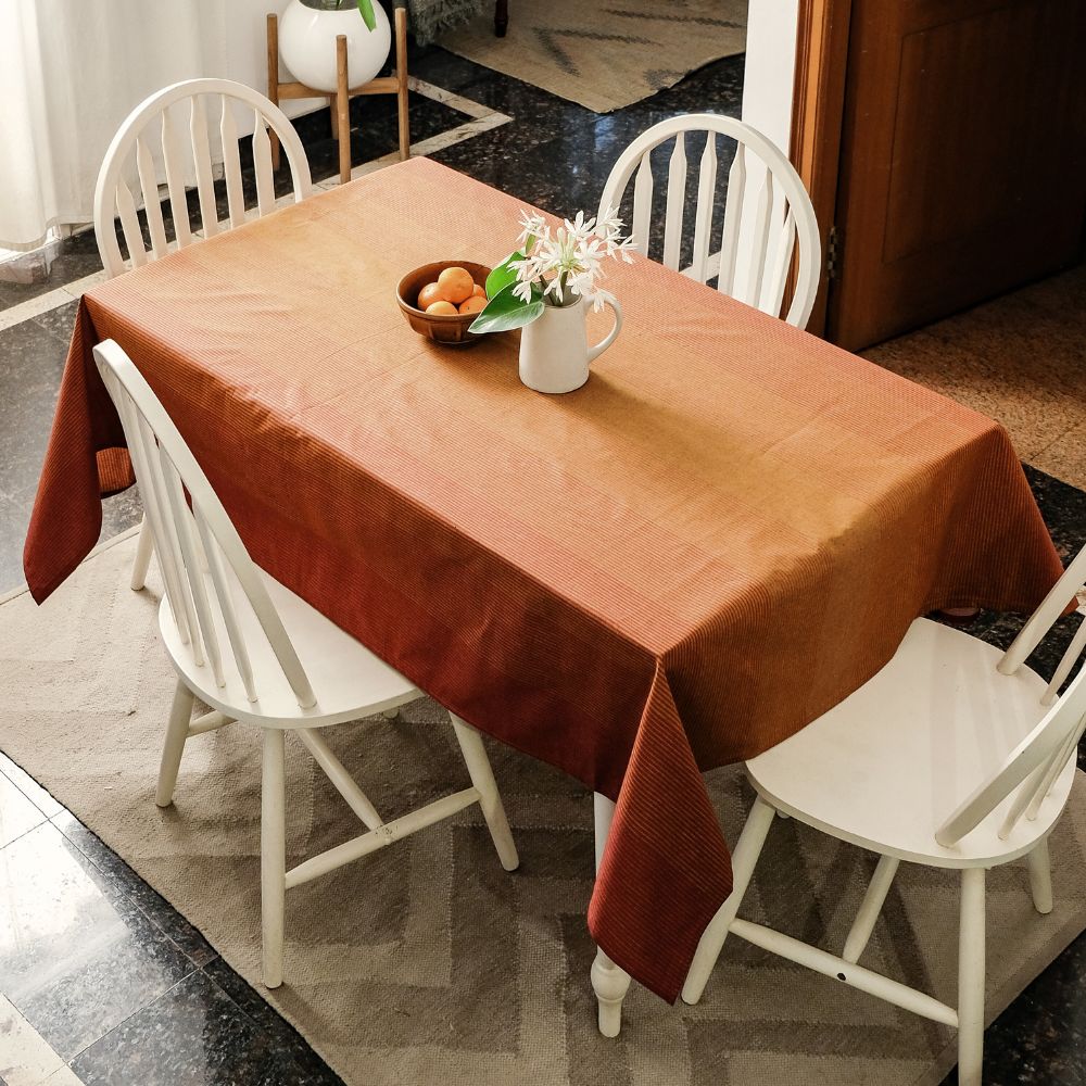Table with a brown tablecloth and white chairs in a room.