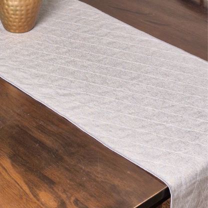 Top view showing the quilted texture of an ochre and white 8 seater reversible runner on a dark wood table.