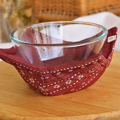 Ruby red reversible pot holder holding a glass bowl, patterned interior lining